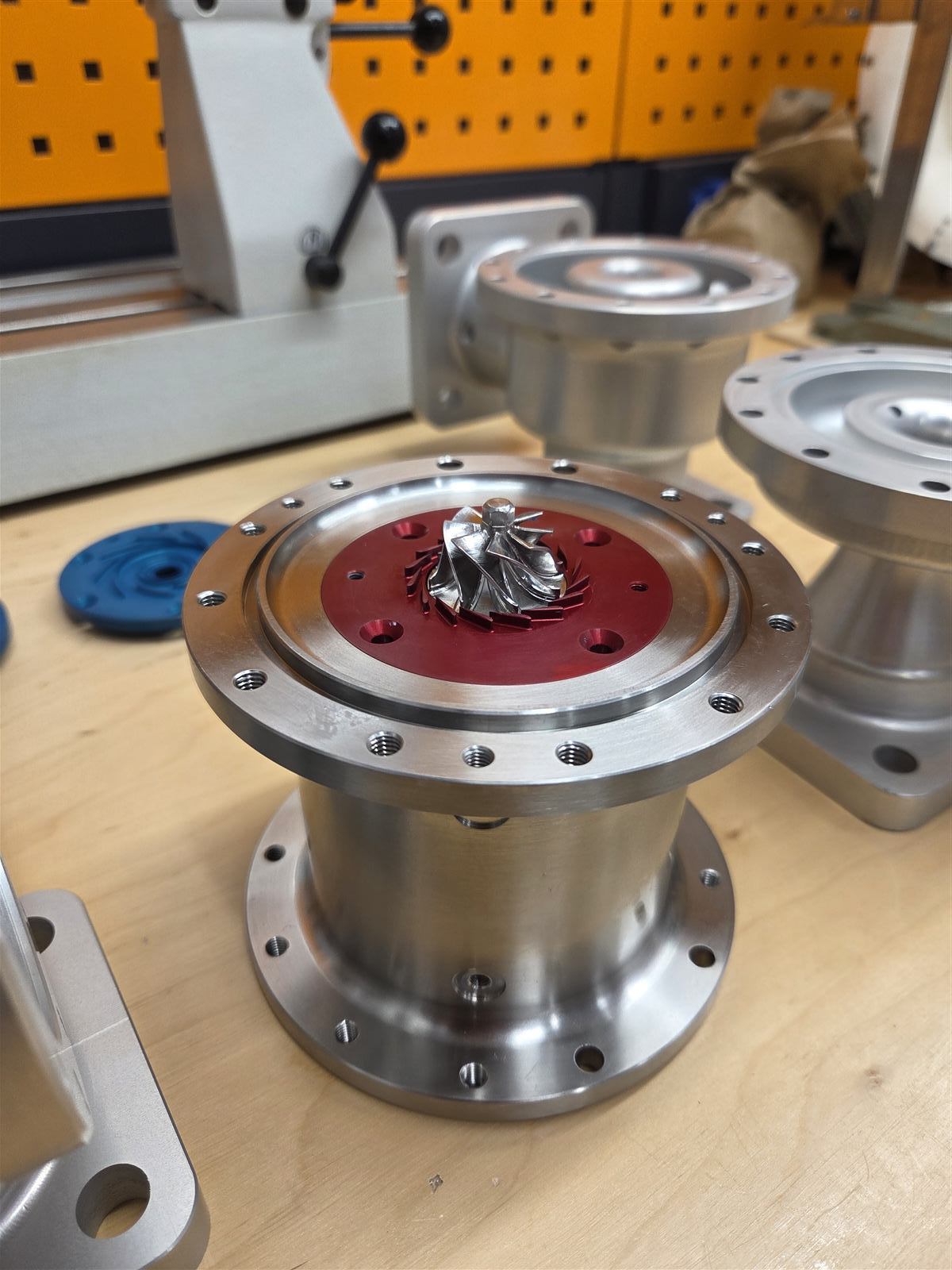 Machined compressor housing with impeller, on a workshop bench alongside other components